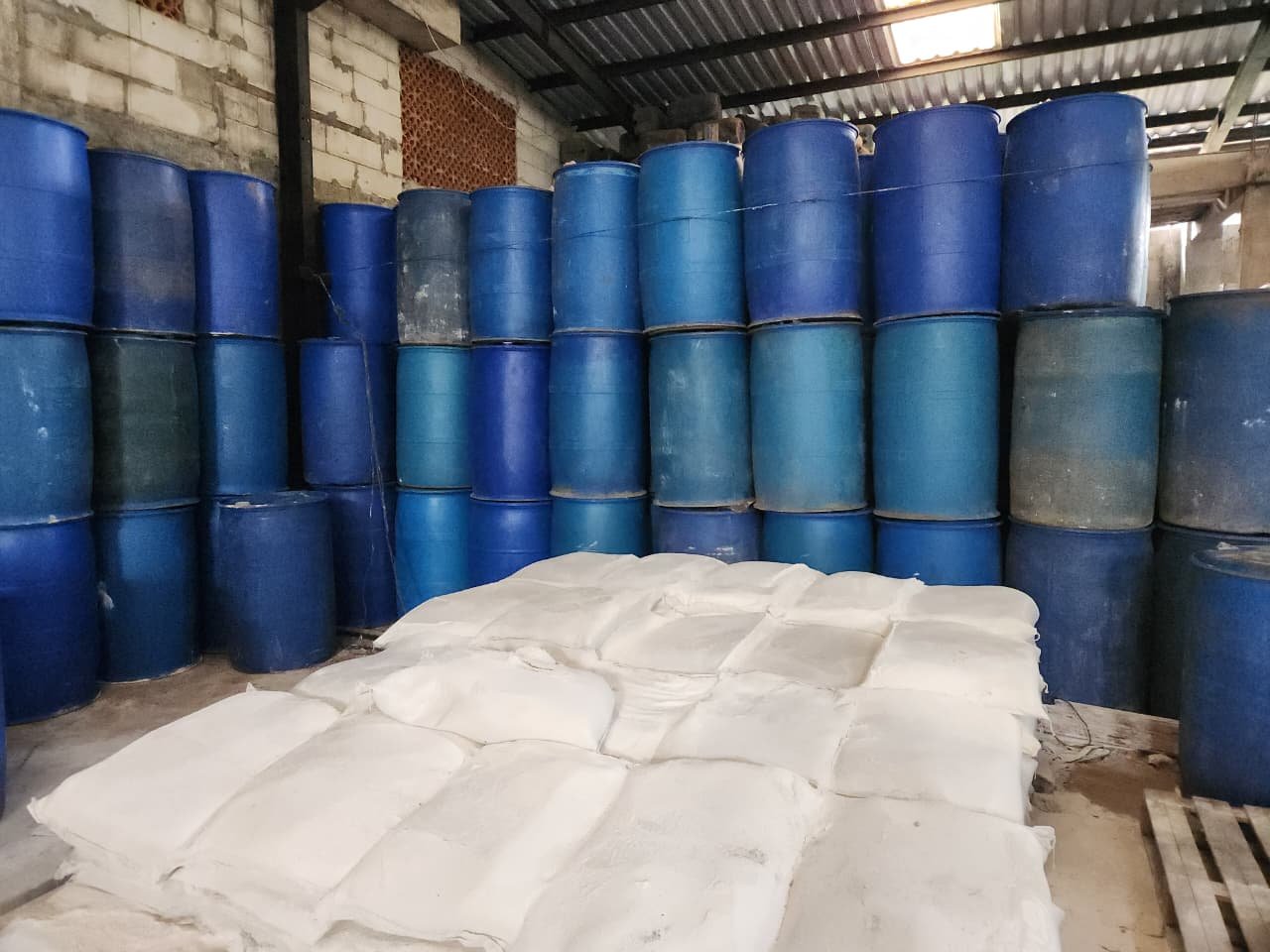 Gudang Magna Kimia: drum biru bertumpuk dan karung bahan kimia di atas palet